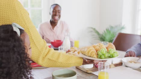 Video-of-happy-african-american-parents,-daughter-and-grandparents-serving-food-and-sitting-at-table