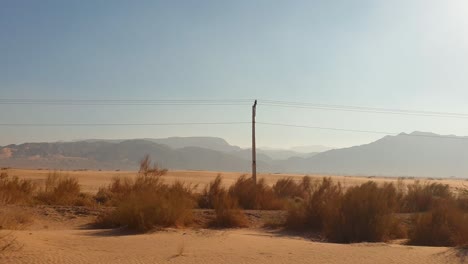 Passing-vast-desert-landscape-near-the-Dead-Sea-with-red-sand,-baron-terrain-and-rugged-mountains-in-distance-in-Jordan,-Middle-East