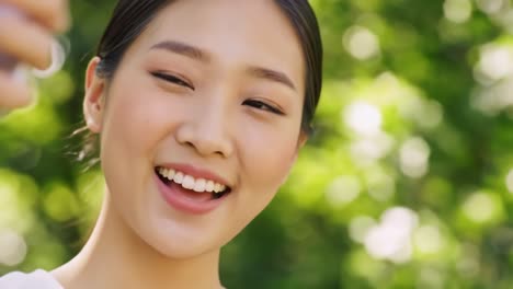 a joyful moment captured: a close-up of a smiling young woman taking a selfie in a lush green environment with sunlight filtering through leaves