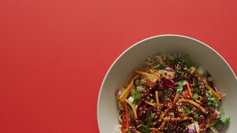 composition of bowl of stir fry noodels with soy sauce and chopsticks on red background