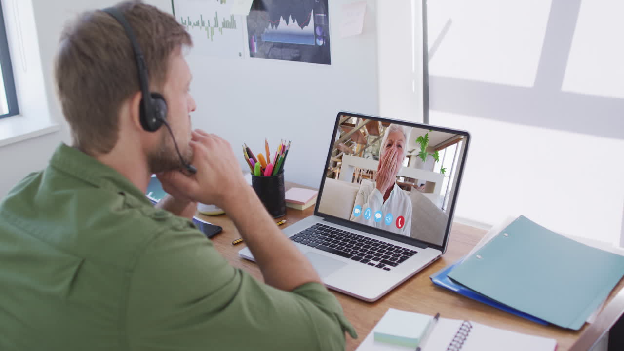 Kaukasisk mand i en videochat på en bærbar computer, iført telefonheadset derhjemme.
