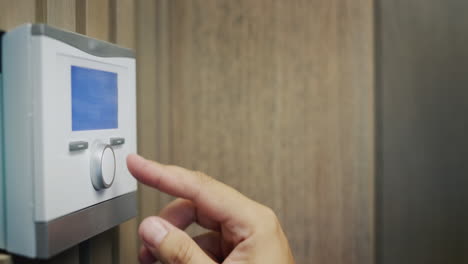 a man adjusts the temperature in the house on a wall-mounted electronic control panel