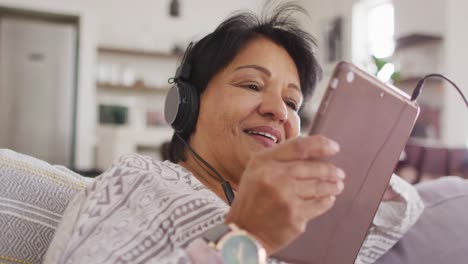 Mujer-Mayor-Afroamericana-Con-Auriculares-Escuchando-Música-En-Una-Tableta-Digital-En-Casa