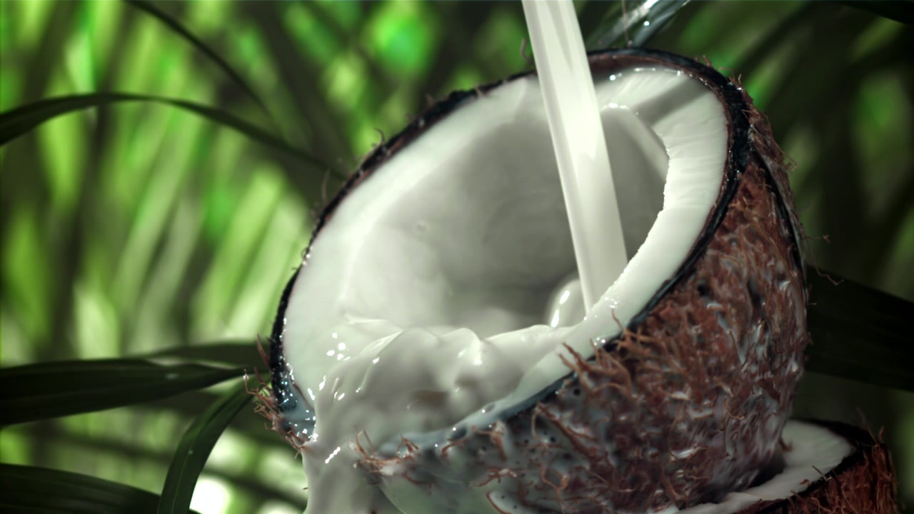 Latte di cocco che si versa in un cocco fresco dimezzato al rallentatore