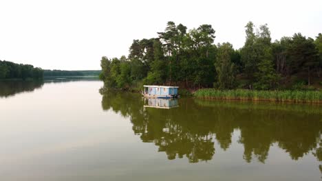 House-boat-floating-on-a-lake-next-to-a-field-of-reed-in-Brandenburg,-Germany