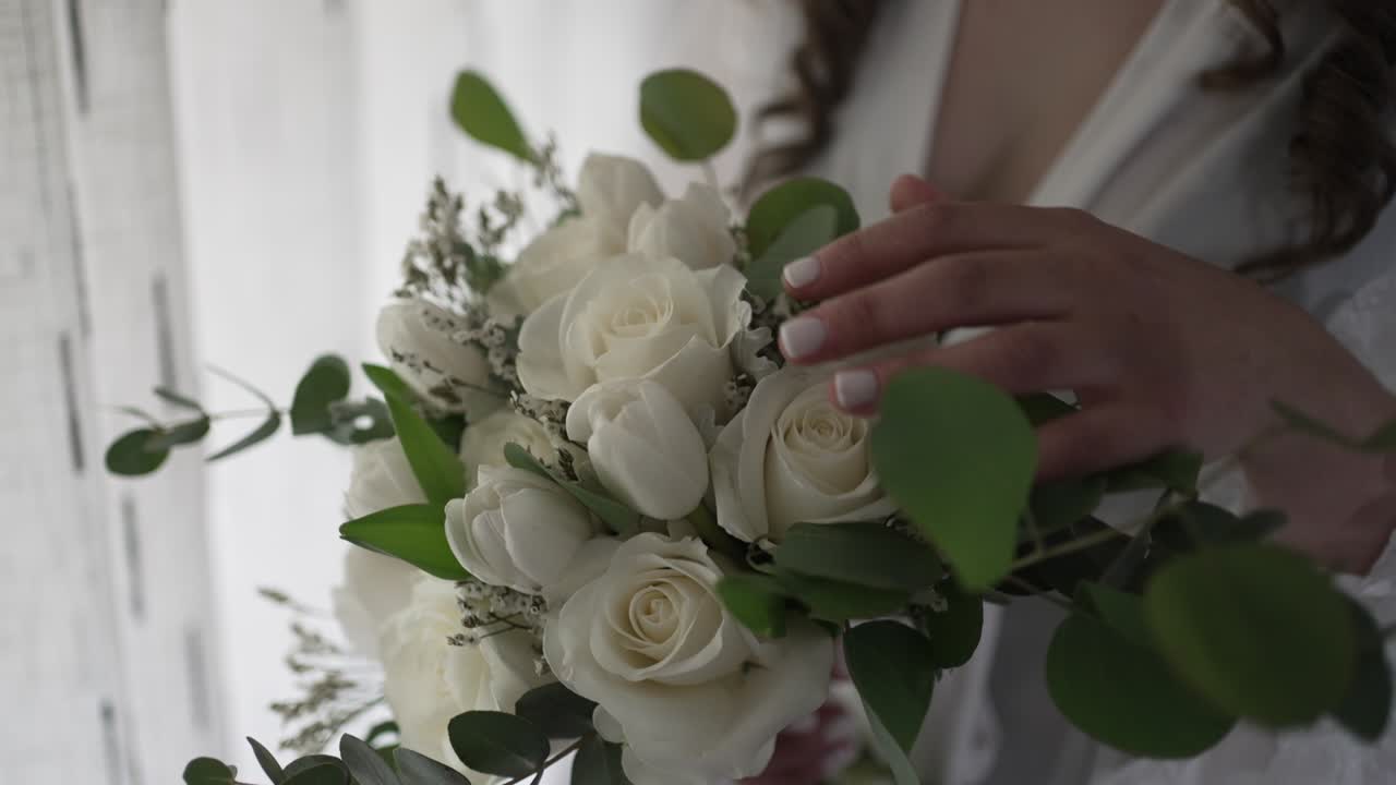 Primo piano di una sposa che tiene in mano eleganti rose bianche con elementi di vegetazione