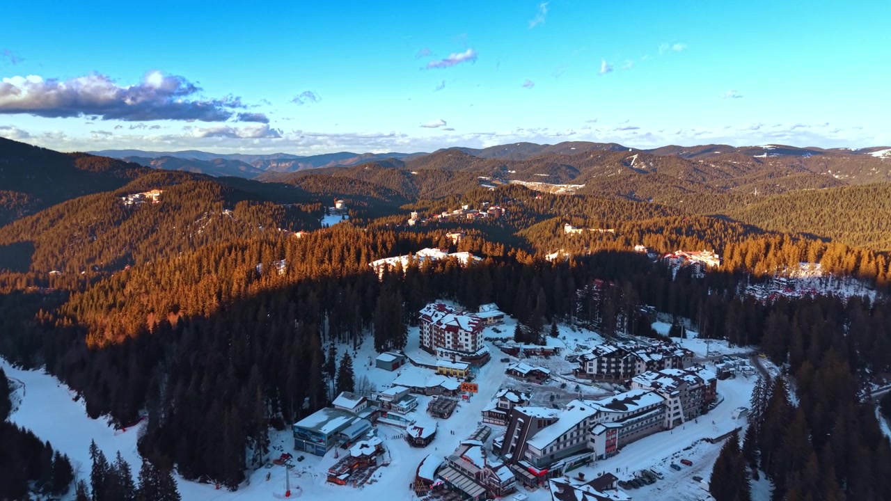 Vista di una località montana invernale. La neve copre il terreno in un resort di montagna immerso in una foresta. Il sole tramonta sulle colline, proiettando ombre sugli edifici.