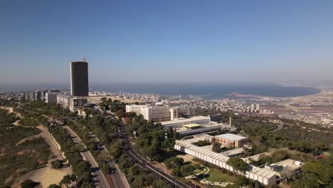 flight to haifa city around a tall building on a hill surrounded by trees and roads, with the harbor and the sea in the background, israel