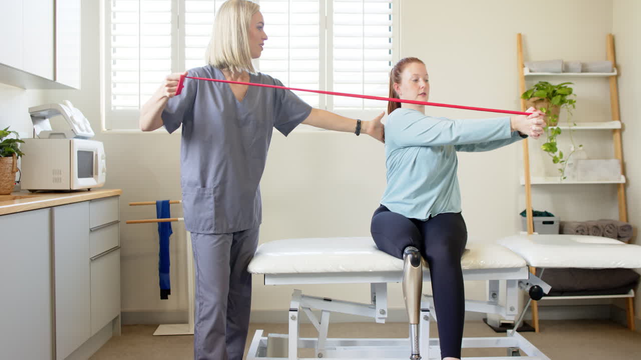 Therapist assisting woman with prosthetic leg using resistance band in clinic