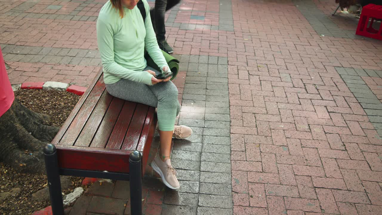 Smartphone che squilla, donna seduta che porta il telefono all'orecchio e risponde a una chiamata su una panca accanto a un tappetino verde