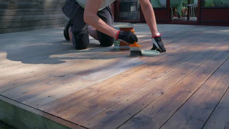 man in workwear use paint brush to apply decking oil to a wooden deck