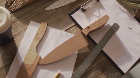 tableta, teléfono inteligente, cuchillos de madera y papeles sobre el escritorio en el taller del fabricante de cuchillos