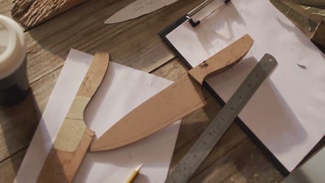 tablet, smartphone, wooden knives and papers lying on desk in knife maker workshop