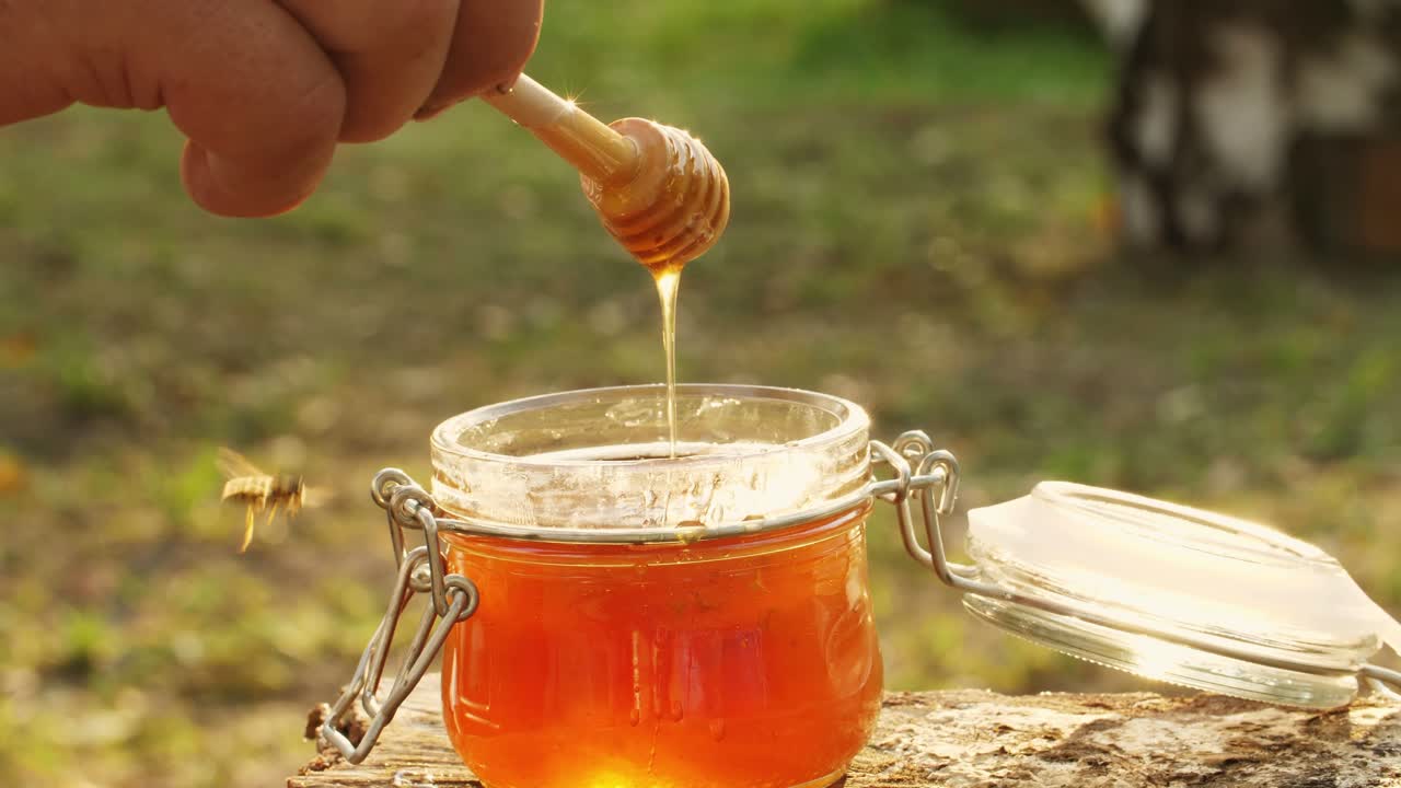 Hand pouring honey from a dipper into a glass jar