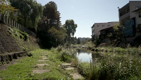 Under-the-daytime-sunshine,-a-serene-scene-unfolds-along-the-path-beside-the-Miyagawa-River-in-Takayama,-Japan