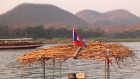 la bandera de laos ondeando en el viento sobre el techo de paja de un barco en luang prabang, laos viajando por el sudeste asiático