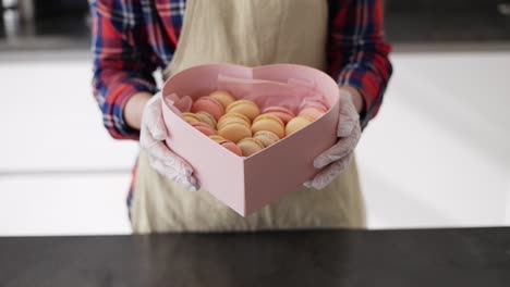 Confectioner-In-Apron-Holding-Box-With-Macaroons-Cookies-At-The-Kitchen