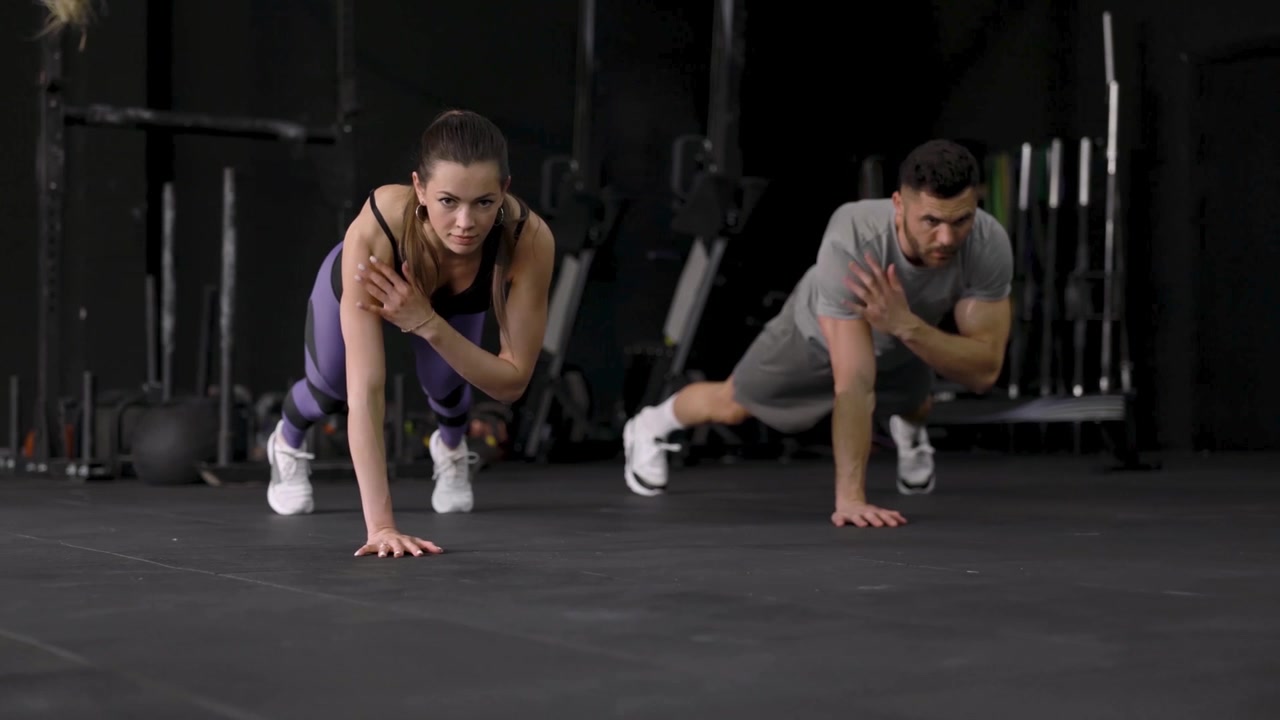 Hombre y mujer en forma realizando planchas con toque de hombro en un gimnasio
