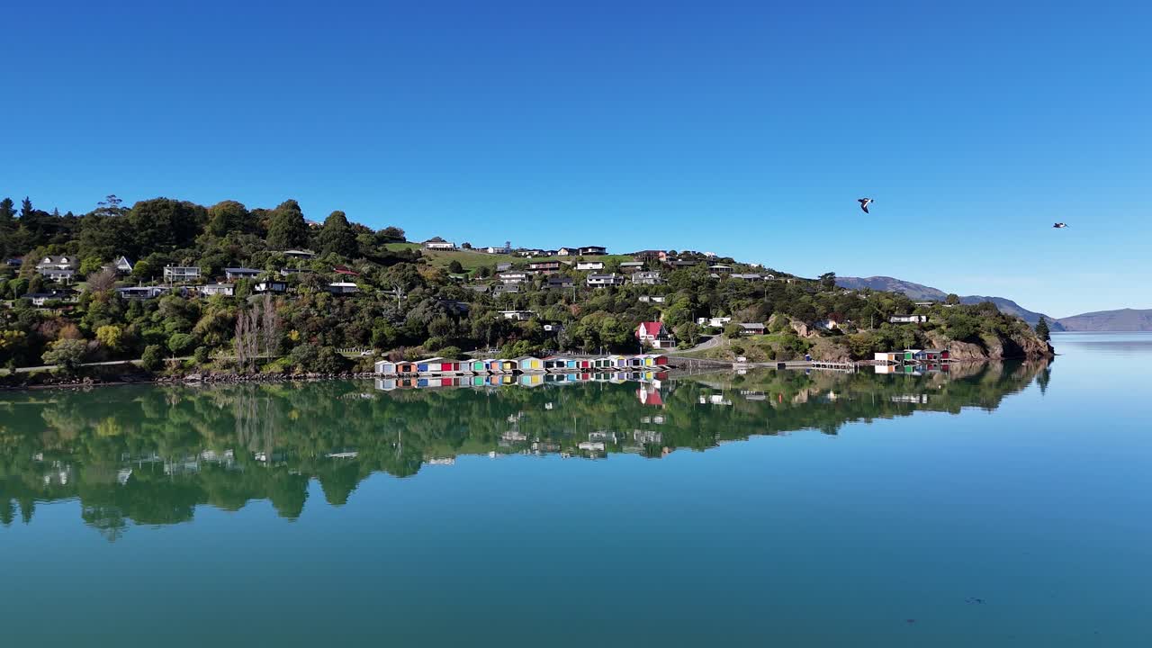 Aerial footage captures calm waters and scenic landscapes of Akaroa Bay under clear blue skies