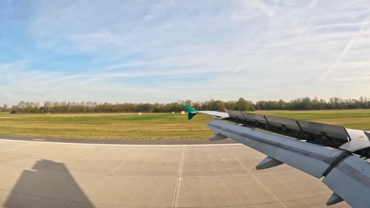 View from airplane window during landing at Munich airport, with wing spoilers deployed and the runway visible
