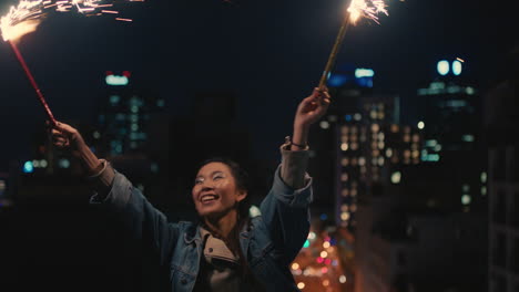 happy young asian woman holding sparklers dancing on rooftop at night celebrating new years eve enjoying holiday celebration