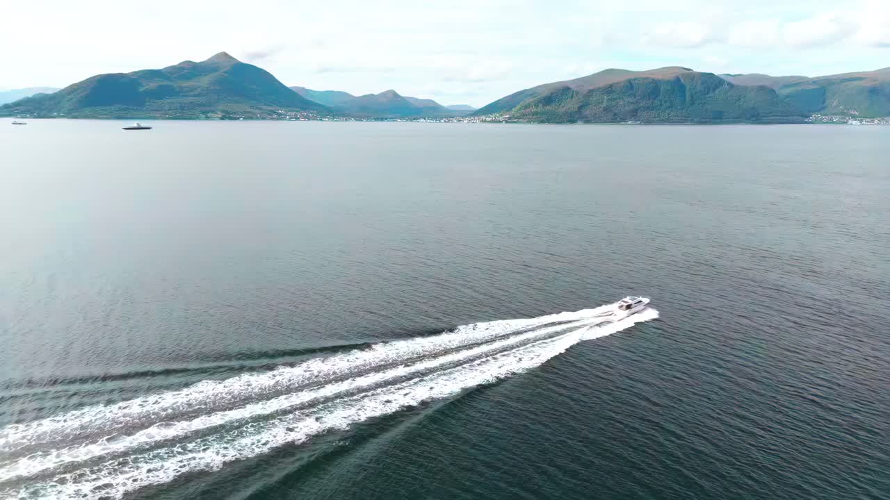 vista aérea de un barco que se desliza a lo largo de las aguas de la costa de nøringset en noruega, con aguas pintorescas y colinas verdes en la distancia