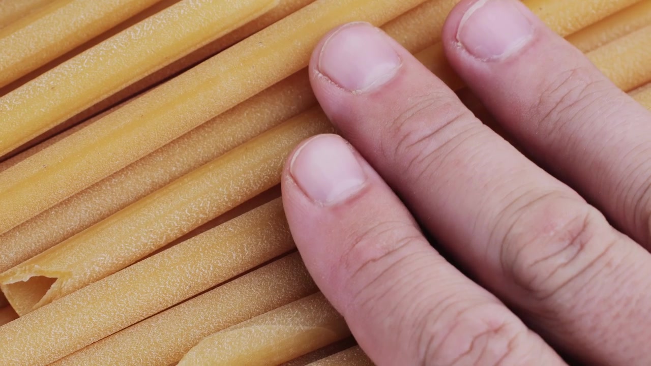 Primo piano di mano che tocca pasta tubolare secca
