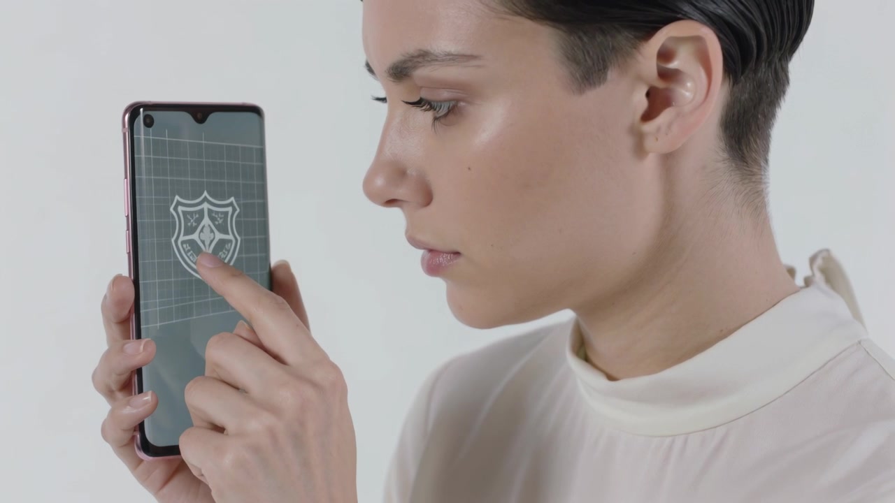 Con il telefono in mano, una modella con un top a collo alto tocca con l'indice in studio, mostrando un emblema a scudo per una dimostrazione.