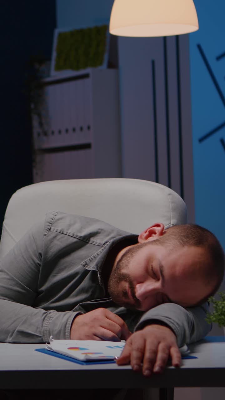 Vertical video Exhausted overworked businessman sleeping on desk table in startup business office