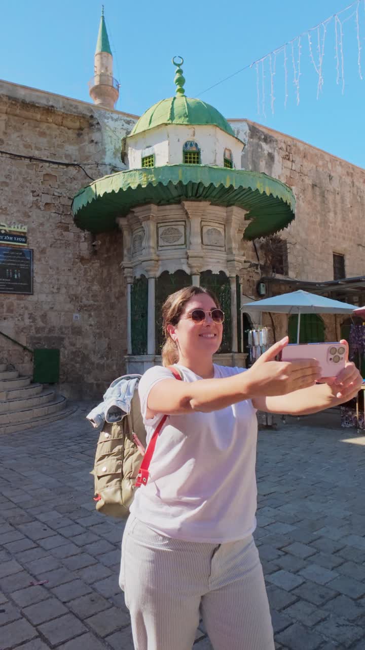 Kvinnelig turist tar en selfie på en solrik, historisk gårdsplass.