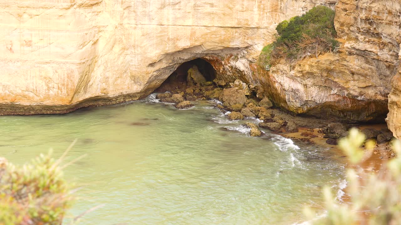 Waves gently lap against the rocky cliffs of Loch Ard Gorge under soft, natural lighting in Port Campbell, Australia