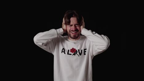 trendy young man covering ears, loud hearing gesture, wide, black background