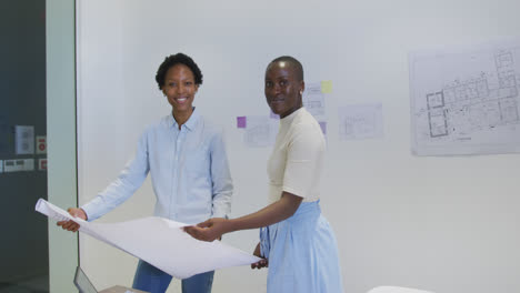 Portrait-of-two-happy-african-american-female-architects-in-discussion-studying-blueprints-in-office