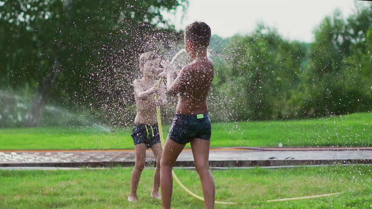 Children play in summer with water pouring from a hose