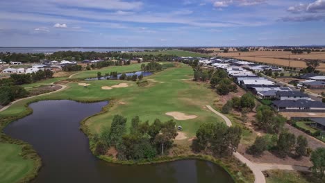 Niedrige-Luftaufnahme-Eines-Fairways-Und-Billabongs-Auf-Einem-Golfplatz-Inmitten-Einer-Neuen-Wohnsiedlung