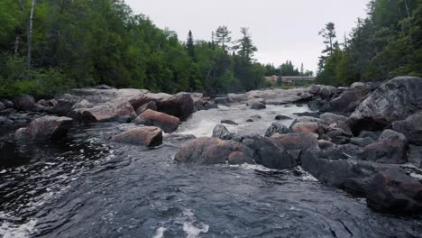 drone footage flying quickly low near the water in a river surrounded by trees in a forest with many rocks and boulders