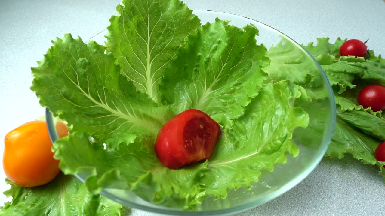 掉落的番茄在生菜葉上。慢動作。