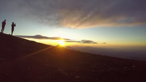 umrissene wanderer machen fotos, um den erfolg der vulkanwanderung bei sonnenaufgang zu feiern