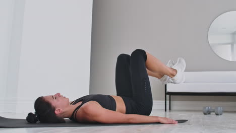 entrenamiento de fuerza peso corporal entrenamiento mujer atleta haciendo patadas de aleteo. mujer europea adulto haciendo ejercicios de piso con elevaciones de piernas para ejercitar los músculos abdominales en casa en su apartamento