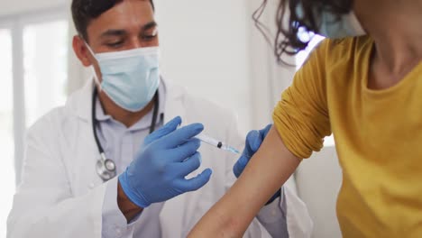 hispanic male doctor making injection to girl at home, all wearing face masks,