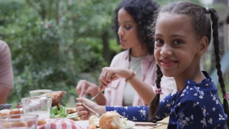 happy biracial parents and daughter eating meal at dinner table in garden, slow motion