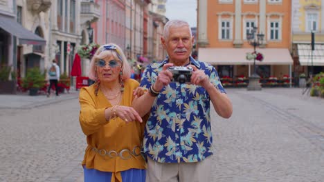 Elderly-stylish-tourists-man-and-woman-taking-photos-with-old-film-camera,-walking-along-city-street