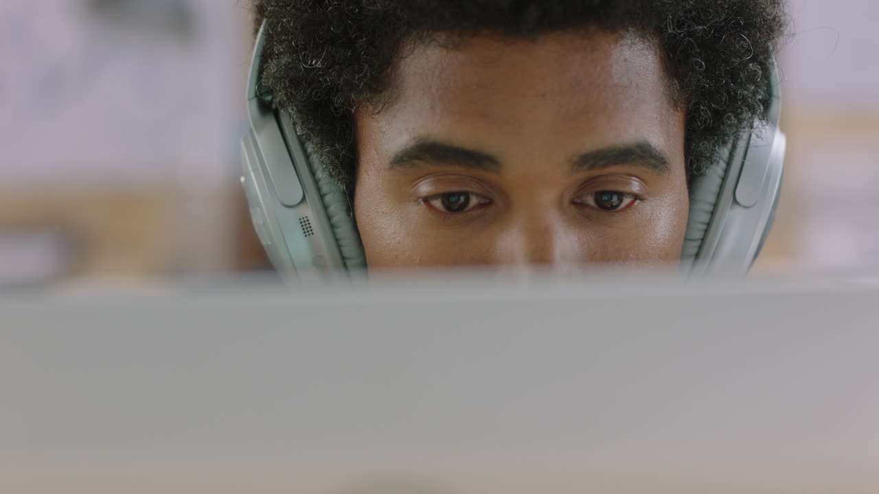 young mixed race businessman using computer working on business project browsing online listening to music brainstorming ideas wearing headphones in relaxed office workplace