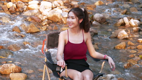 asian woman in red sitting on a chair with big rocks and water slow splashing for relaxing and happiness in the vacation summertime