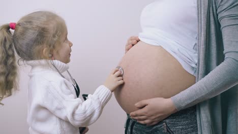 chica feliz juega al médico con mamá embarazada en la pared blanca
