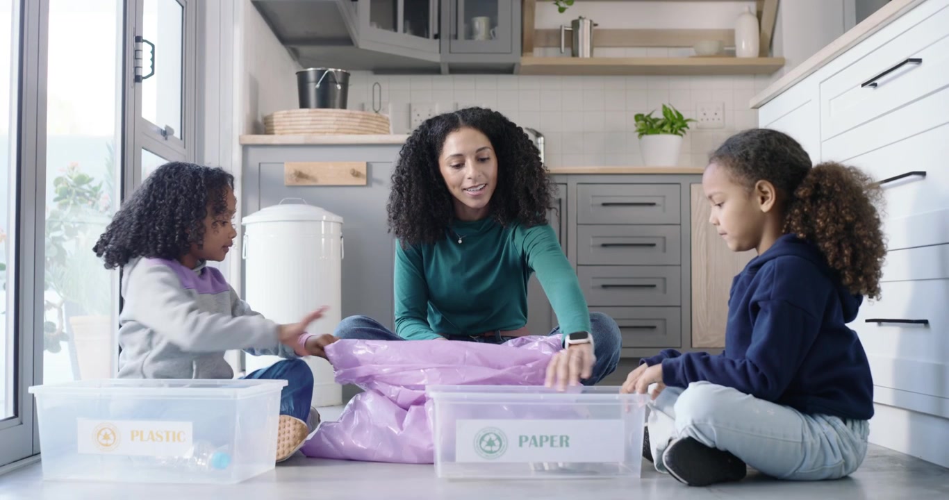 African American mom and girls sorting purple bag in kitchen into PLASTIC or PAPER bins for recyclin