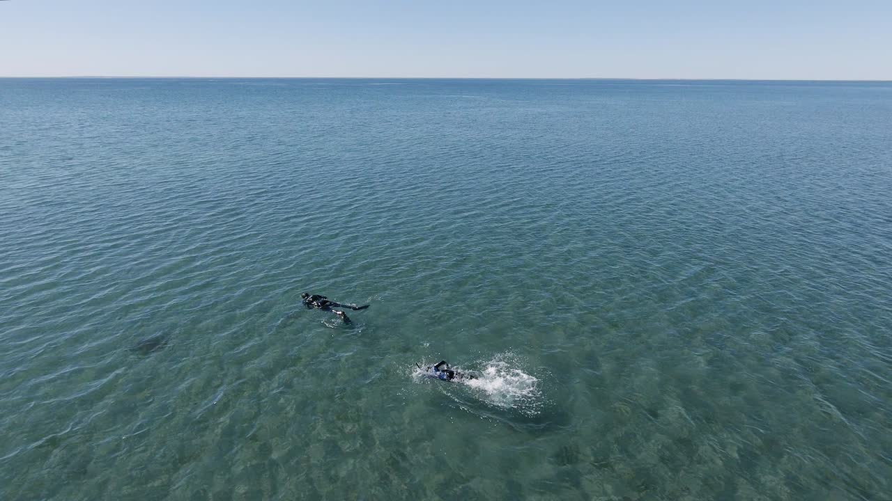 Two People In Wetsuits Swimming In The Rippling Blue Sea In Villarino Beach On A Sunny Day - aerial