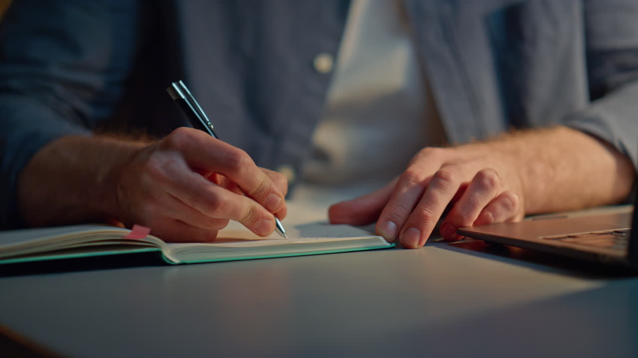 Man hands writing notebook at late office closeup. Anonymous guy making notes
