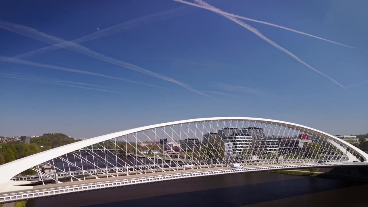 Low angle view of the modern white Troja Bridge in Prague spanning the Vltava river with a cyclist on a riverside path under a sunny blue sky