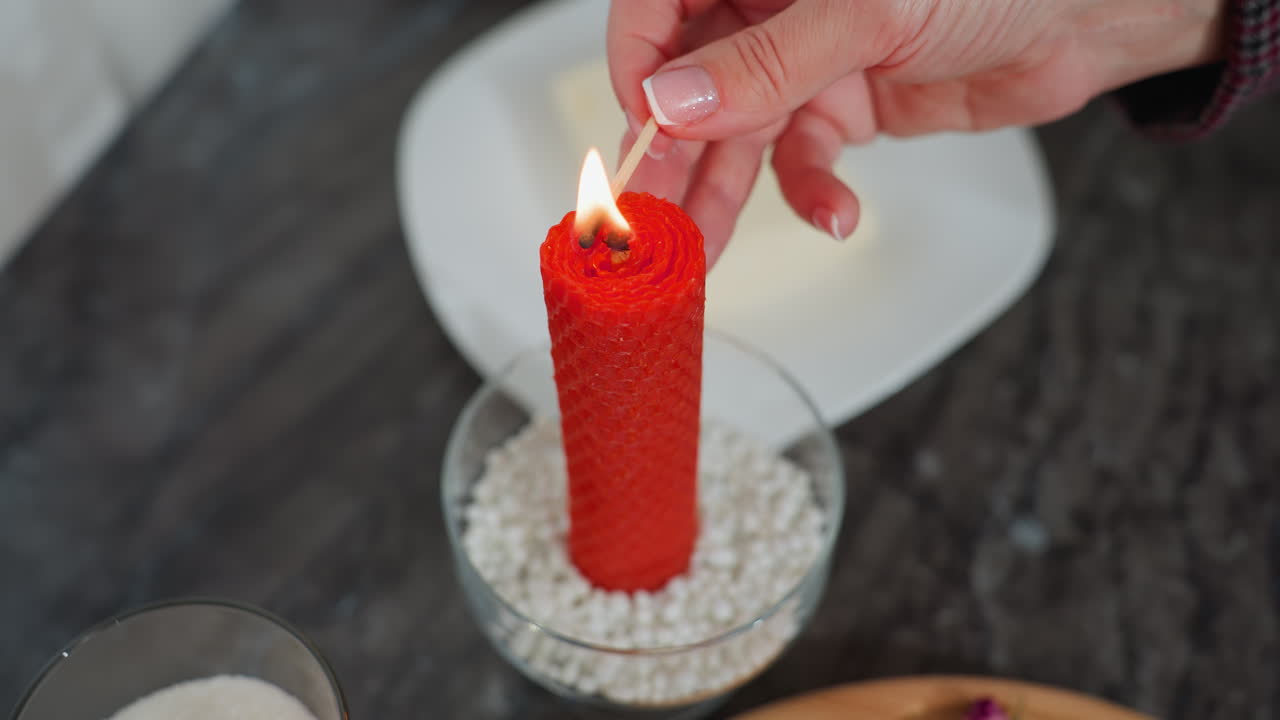 vista de arriba hacia abajo de la mano encendiendo vela roja con cerilla en la mesa de la cocina, ambiente acogedor y cálido con varios artículos de cocina que rodean la configuración